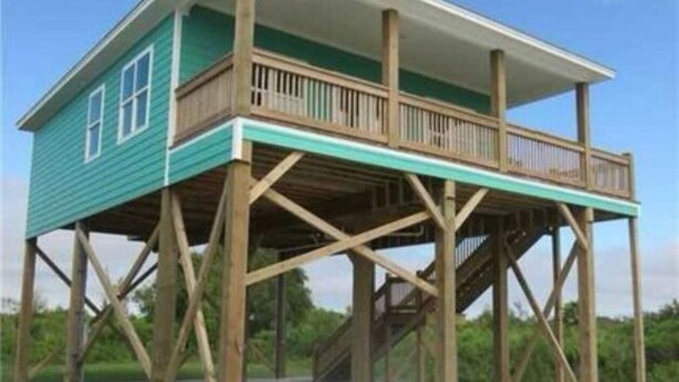 Een houten terrasconstructie met een balkon, ondersteund door houten balken.
