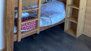 Una cama litera con estructuras de madera y estantes, un cojín con estampado de oso, y un objeto negro pequeño en el techo.