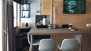 Una cocina moderna con encimera de madera, dos sillas grises, un televisor montado en la pared y un estante con varios objetos.