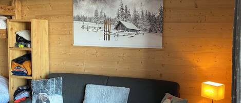 Een gezellige woonkamer met een grijze bank, houten planken, een aan de muur hangend schilderij van een besneeuwd berglandschap en een tafellamp.