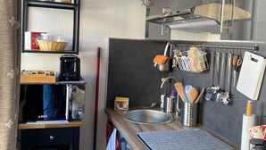 Una cocina compacta con microondas, cafetera y un colgador para utensilios.
