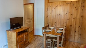 Ett litet rum med ett matbord och stolar i trä, en tv-apparat placerad på ett träskåp och en dörr som leder till ett annat rum.