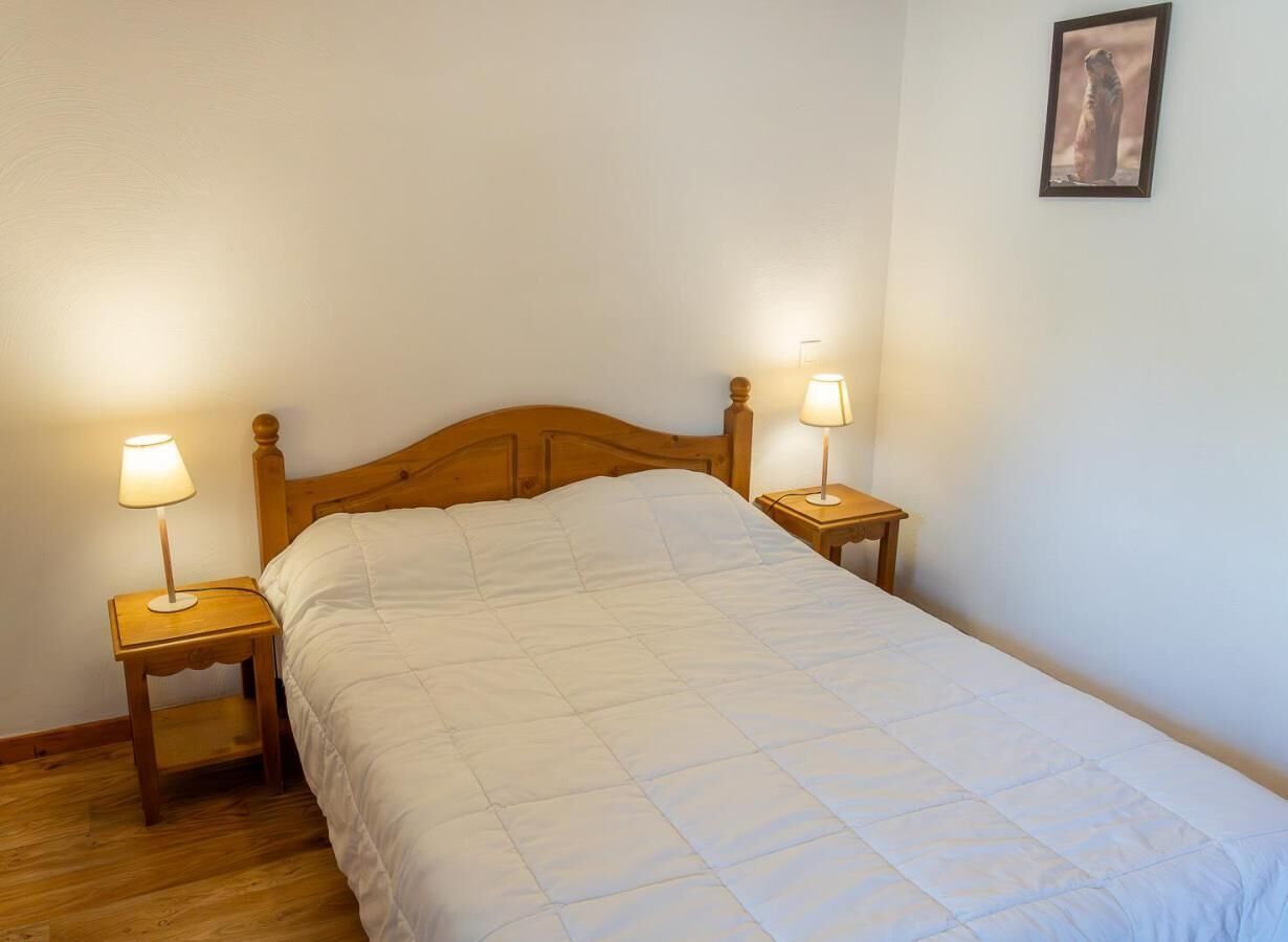 A single bed with a wooden headboard, flanked by two bedside tables with lamps, in a room with plain walls and a wooden floor.