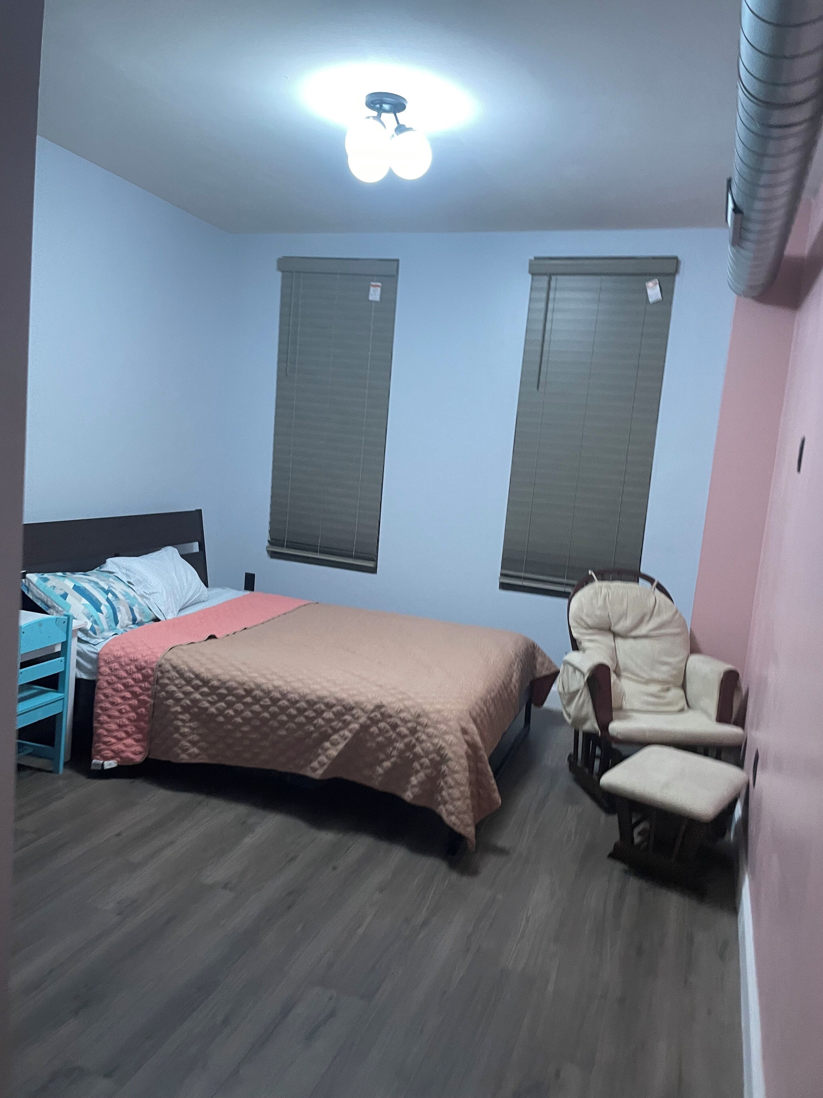 A bedroom with a bed, a chair, a window, and a ceiling light.