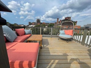 A wooden deck with a sofa, a wicker chair, and a table. - Marble Hill Manor (Baltimore)