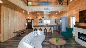 Un vaste espace de vie doté d’un haut plafond, de murs en bois, d’un îlot central avec des tabourets de bar, d’un canapé, d’une table basse ronde et d’une cheminée.
