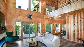 Un intérieur spacieux en bois, avec un canapé incurvé, une cheminée et de grandes fenêtres offrant une vue sur l’extérieur.