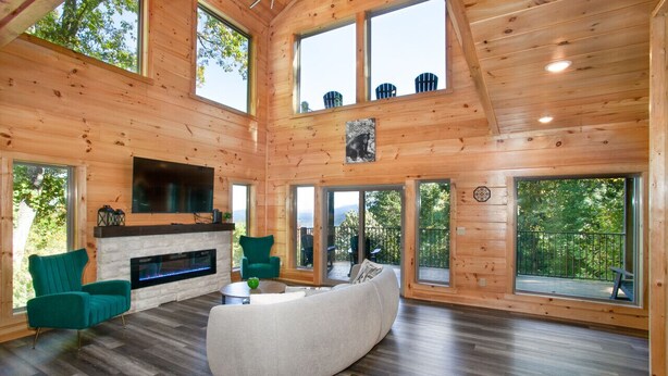 Une cabane en bois spacieuse, dotée d’une cheminée, de grandes fenêtres et d’un coin salon confortable.