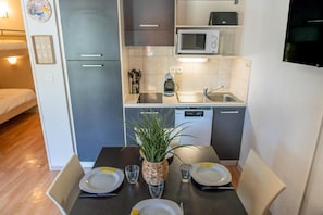 A compact kitchen with a microwave, sink, and dishwasher. There is a dining table set with plates, glasses, and a potted plant.