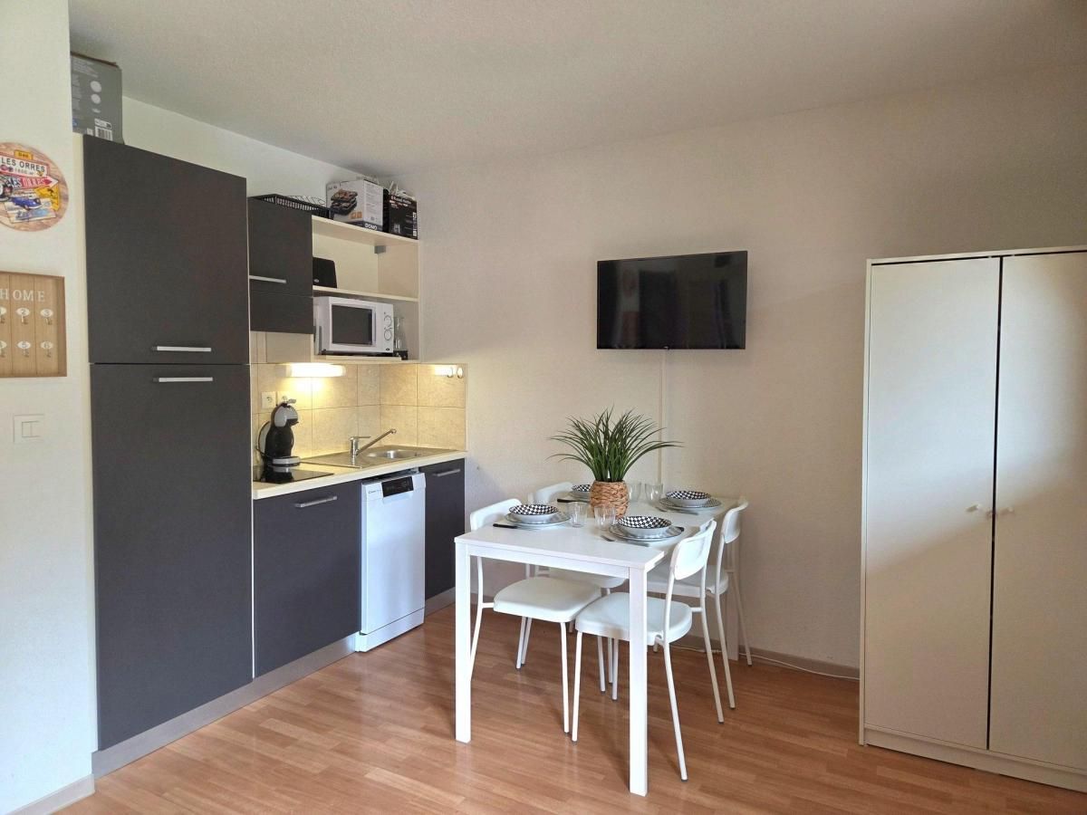 A compact kitchen with a dining area, a microwave, a sink, and a flat-screen TV mounted on the wall.