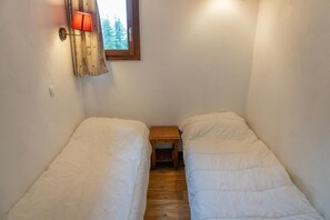 Une petite chambre agréable, dotée de deux lits simples, d’une petite table de chevet en bois et d’une lampe fixée au mur.