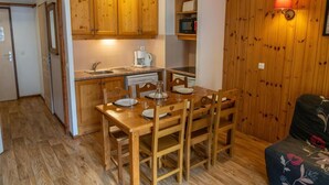 Une cuisine compacte avec des meubles en bois, une table à manger avec des chaises, un four à micro-ondes et une machine à café.