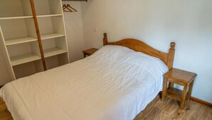 Une chambre à coucher avec un lit en bois, une table de chevet en bois, une armoire en bois et une étagère en bois.