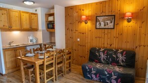 Une cuisine compacte avec des meubles en bois et une table à manger pour quatre personnes. Un canapé à motifs floraux est placé contre un mur en bois.
