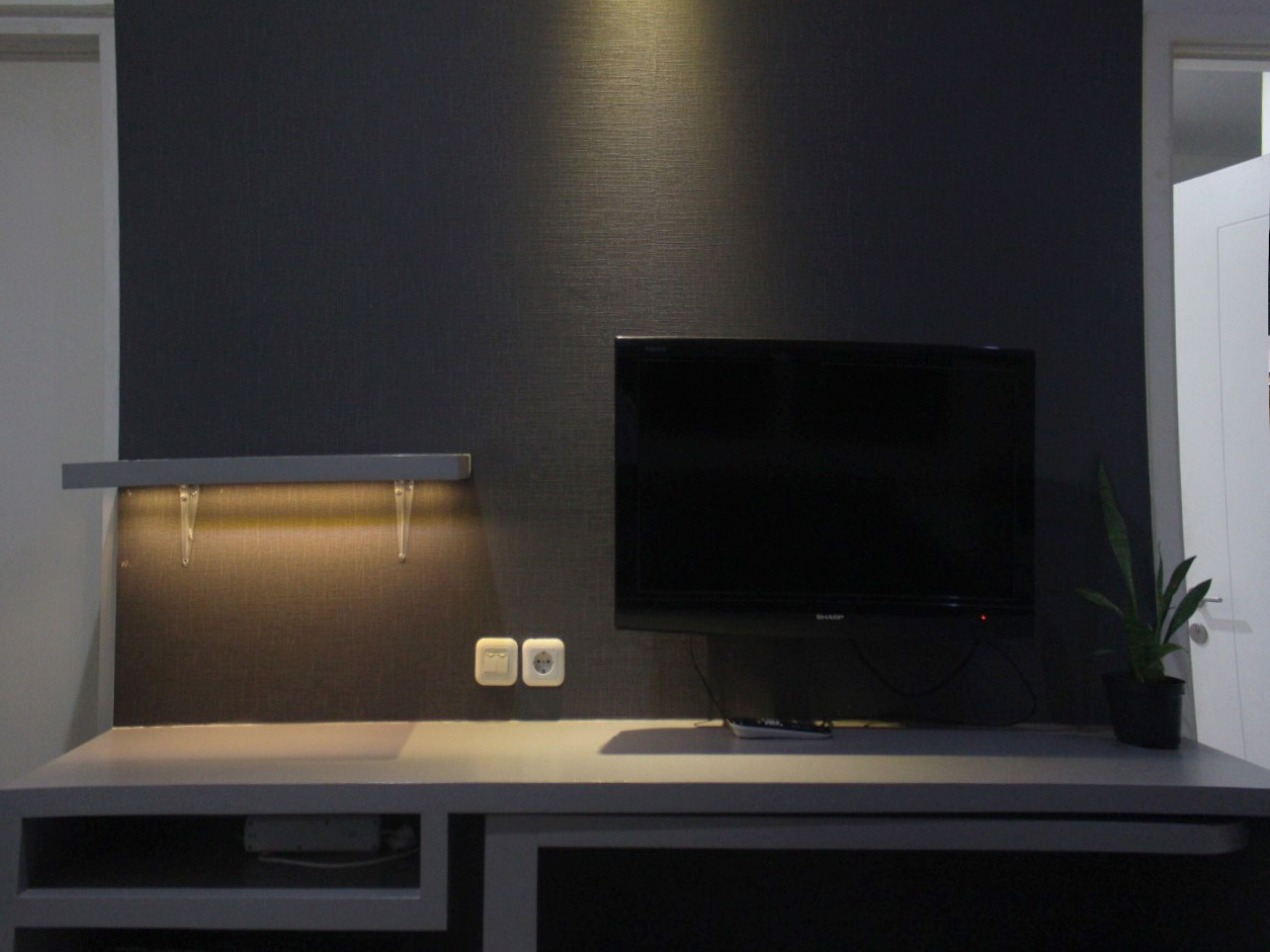 Un meuble de rangement moderne pour appareils multimédias, doté d’un téléviseur à écran plat, d’une étagère et d’une petite plante.