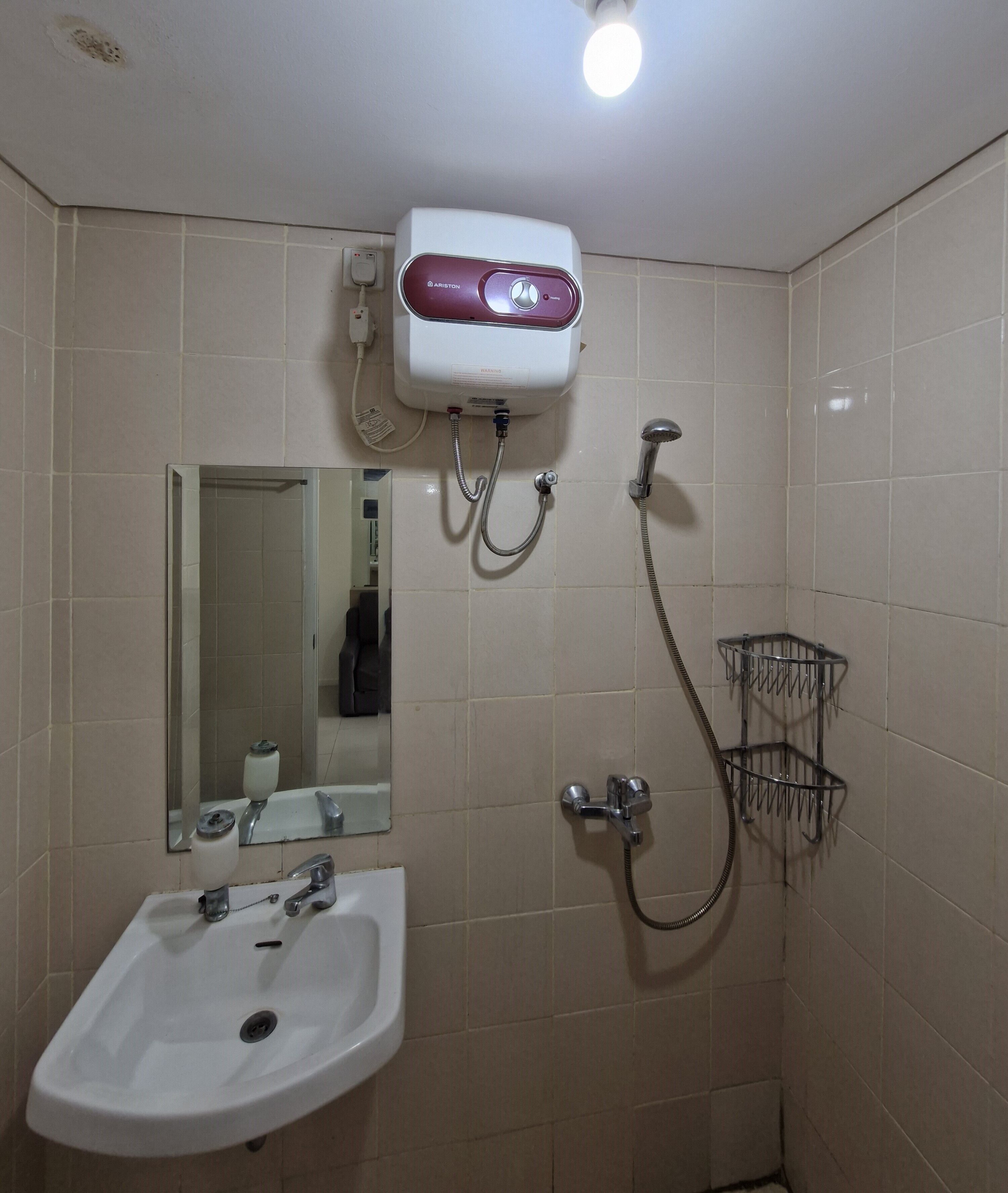 Un bagno con lavandino bianco, uno specchio, un soffione a mano e un porta carta igienica a muro.