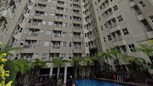 Een hoog appartementencomplex met verschillende balkons en een zwembad aan de voet ervan.