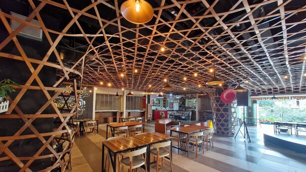 Een restaurant met een geometrisch houten plafond, houten tafels en stoelen, en uitzicht op het buiten.