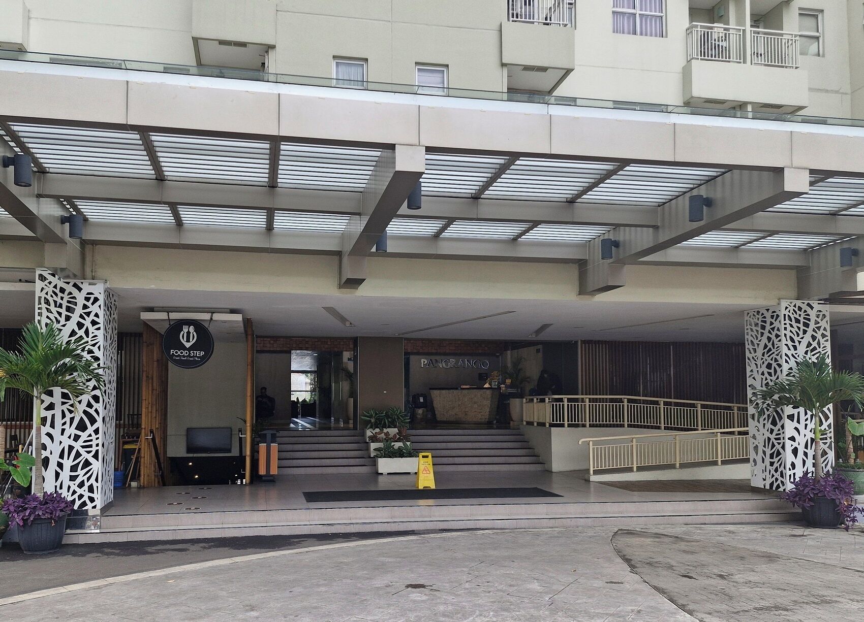 L’entrée d’un hôtel, avec un espace abrité, un comptoir d’accueil et un escalier menant aux étages supérieurs.