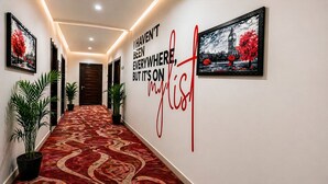 A hallway with patterned carpet, potted plants, framed artwork, and a wall with a motivational quote. - Hotel Grand Regency by JMD Group (New Delhi)