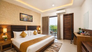 A hotel room with a large bed, a desk, a chair, a small table, a potted plant, and a painting on the wall. - Hotel Grand Regency by JMD Group (New Delhi)