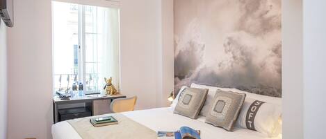 Un dormitorio con cama, escritorio, silla, ventana y un mural de nubes en la pared.