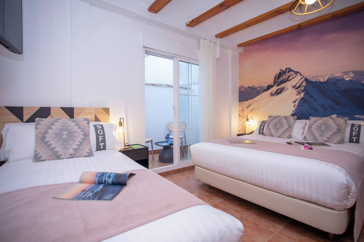 Une chambre d’hôtel avec deux lits, une fresque murale représentant un paysage de montagne et une porte-fenêtre coulissante donnant sur le balcon.