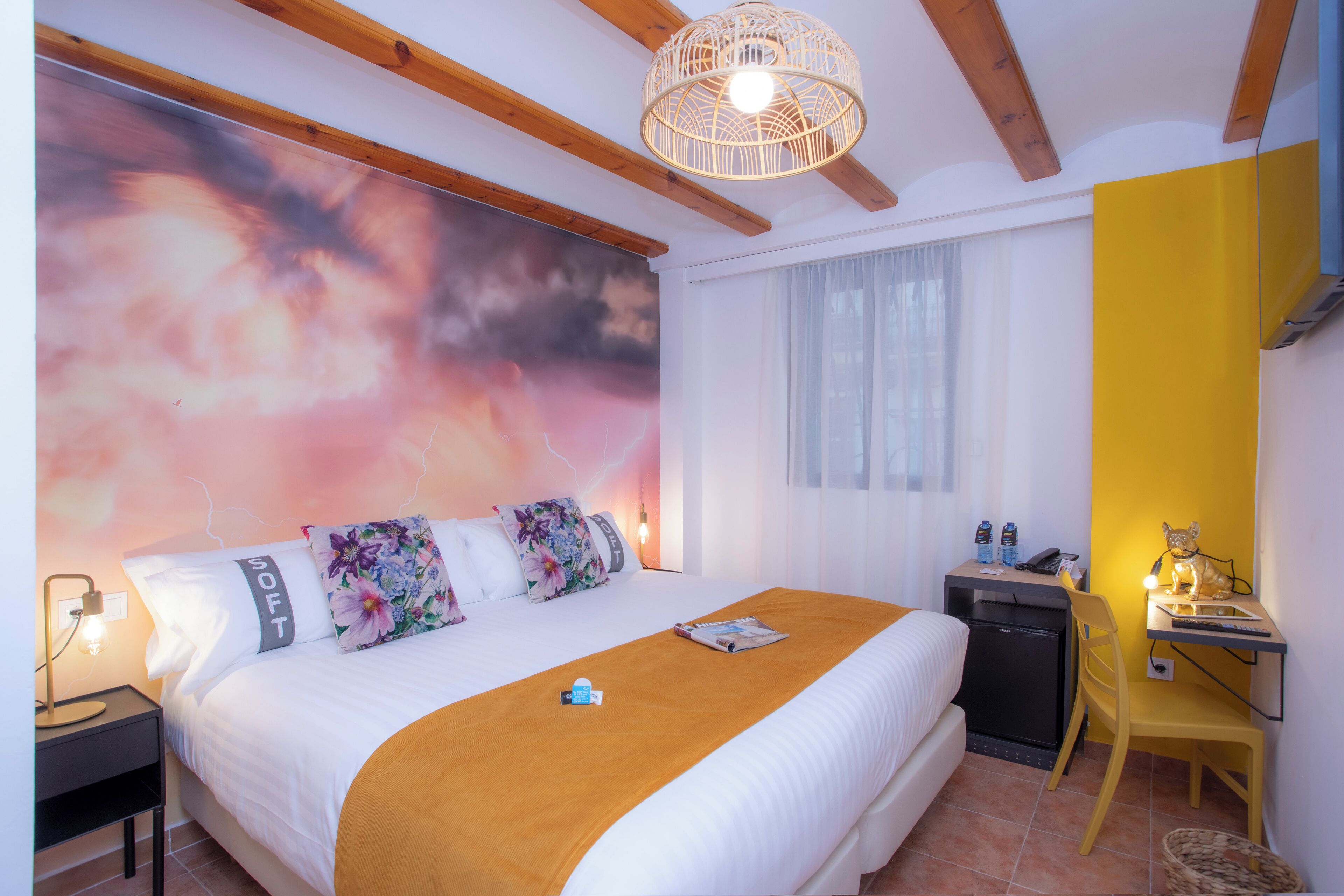 A bedroom with a bed, bedside table, lamp, and a desk with a chair.