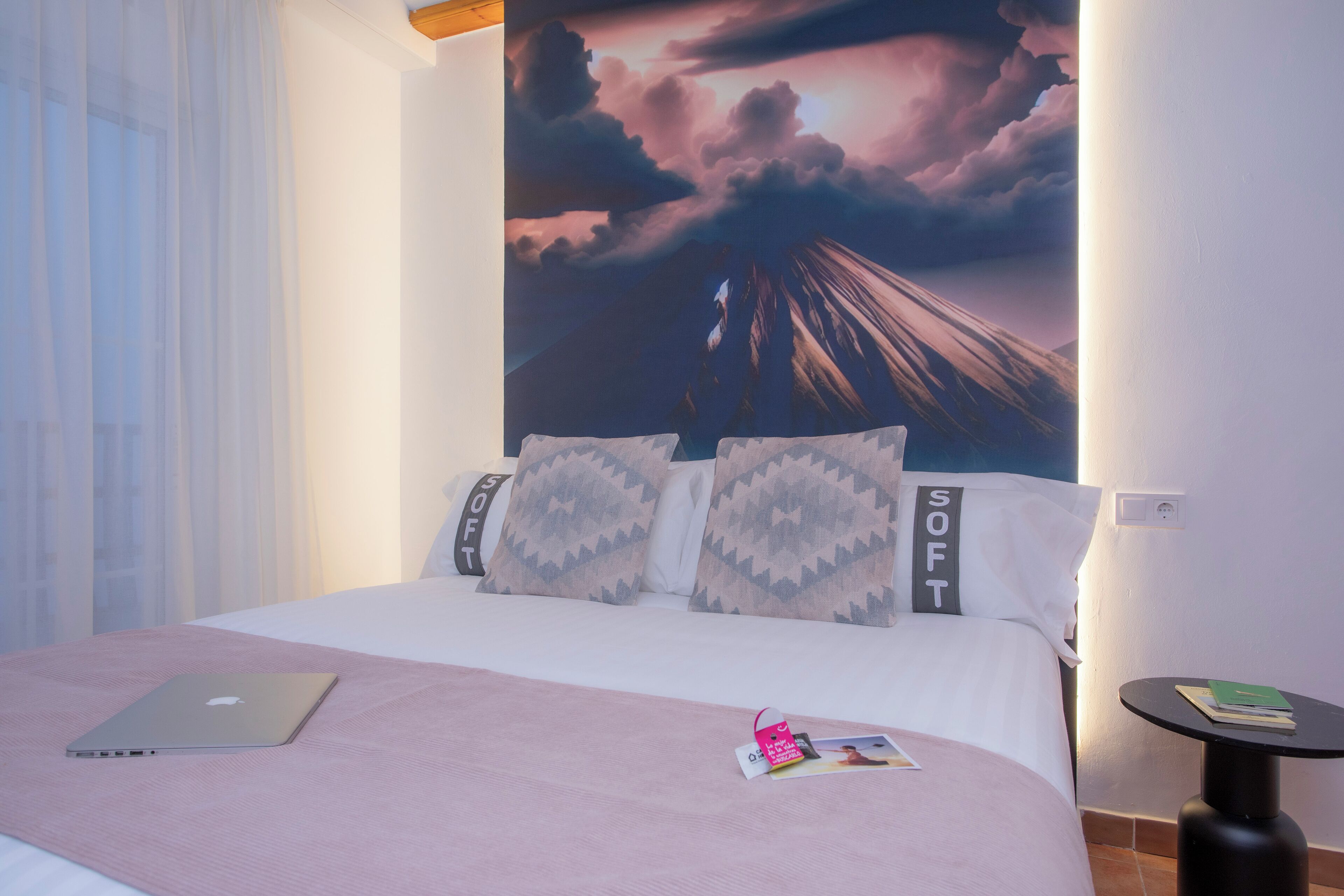 Une chambre d’hôtel avec un lit, un ordinateur portable, une petite table et un mur orné d’un grand tableau.