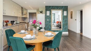 A modern kitchen with a dining area, featuring a round wooden table, green upholstered chairs, and a vase with flowers. - Apartment in Guildford with Parking (Guildford)