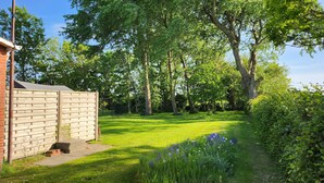 A well-maintained garden with a brick structure, lush green grass, and various flowering plants. - Large family vacation apartment (100 m²) near SPO - dogs welcome 1000m2 garden (Poppenbüll)