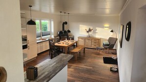 A modern kitchen with wooden cabinets, a dining table set for four, and a cozy seating area with a chair and bench. - Large family vacation apartment (100 m²) near SPO - dogs welcome 1000m2 garden (Poppenbüll)
