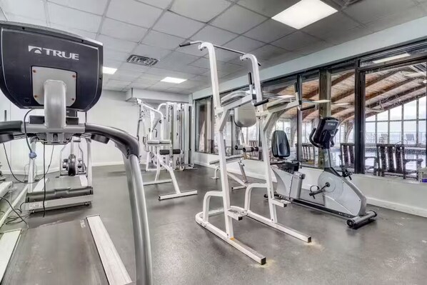 Une salle de sport équipée de divers appareils d’exercice, d’un tapis de course et de grandes fenêtres donnant sur l’extérieur.
