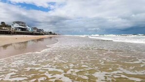 Une plage avec des vagues, un ciel nuageux et une maison sur la gauche.