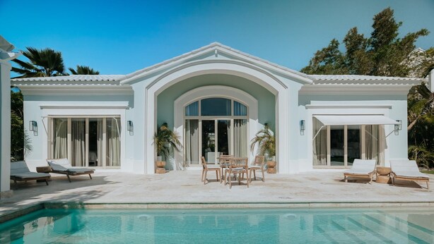 Una casa moderna con piscina, ventanas amplias y mobiliario exterior.
