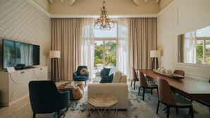 Amplia sala de estar con televisor, asientos cómodos, comedor y ventanas grandes con vistas al exterior.