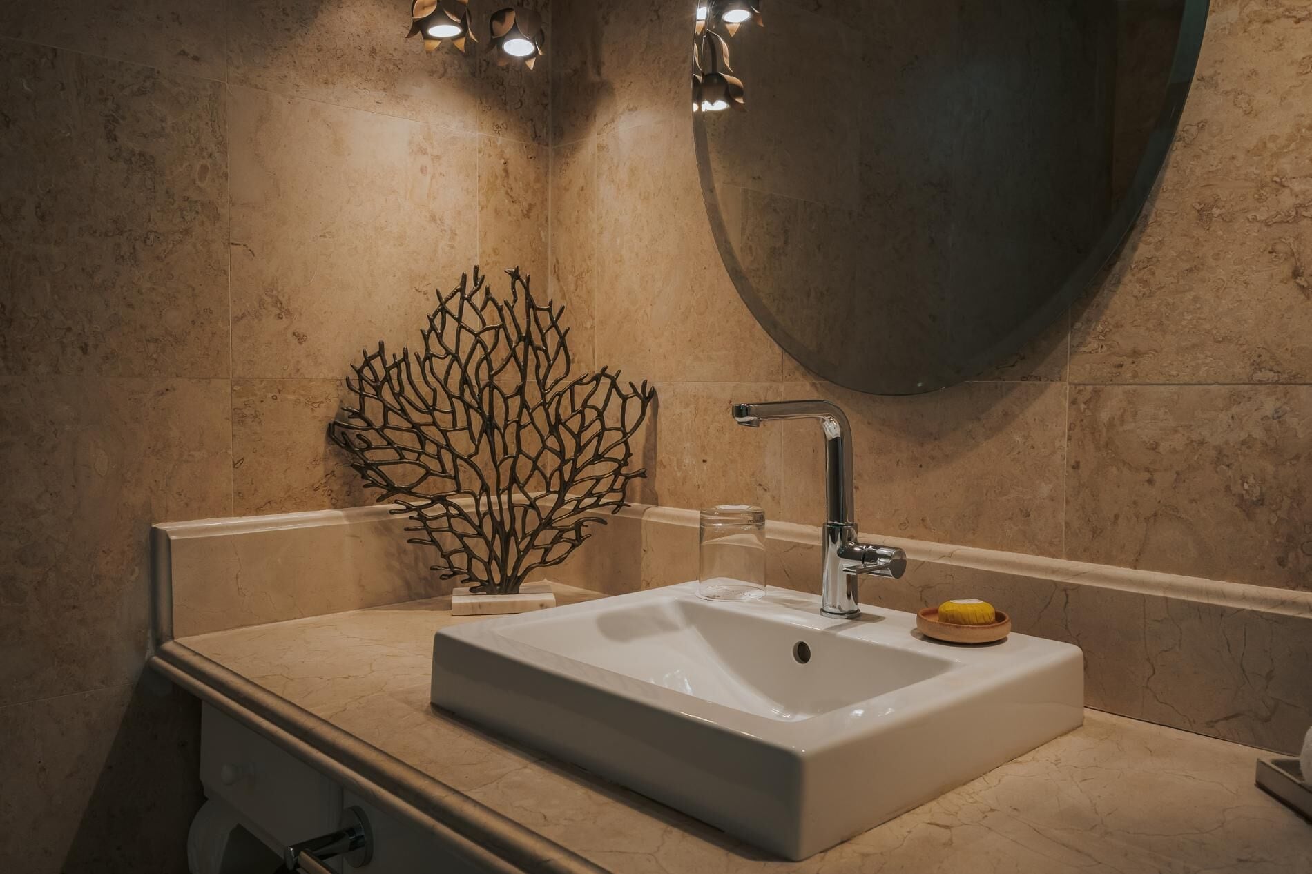 Ein Badezimmer mit einem weißen Waschbecken, einem modernen Wasserhahn und einem dekorativen Korallenstück auf der Ablagefläche.