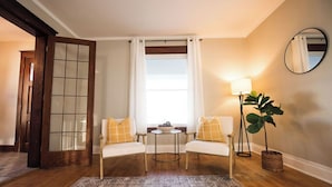 A cozy room with two white armchairs, a small round table, a lamp, and a large plant.