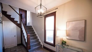 A staircase with wooden railings and a chandelier, a white door, and a window with a view.