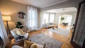 A spacious living room with a large rug, a sofa, a chair, and a dining area with a table and chairs.