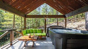 Een overdekt terras met een hottub, houten meubels en uitzicht op het bos.