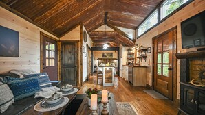 Een gezellig chaletinterieur met een houten plafond, een eethoek met kaarsen, een keuken en een open haard.