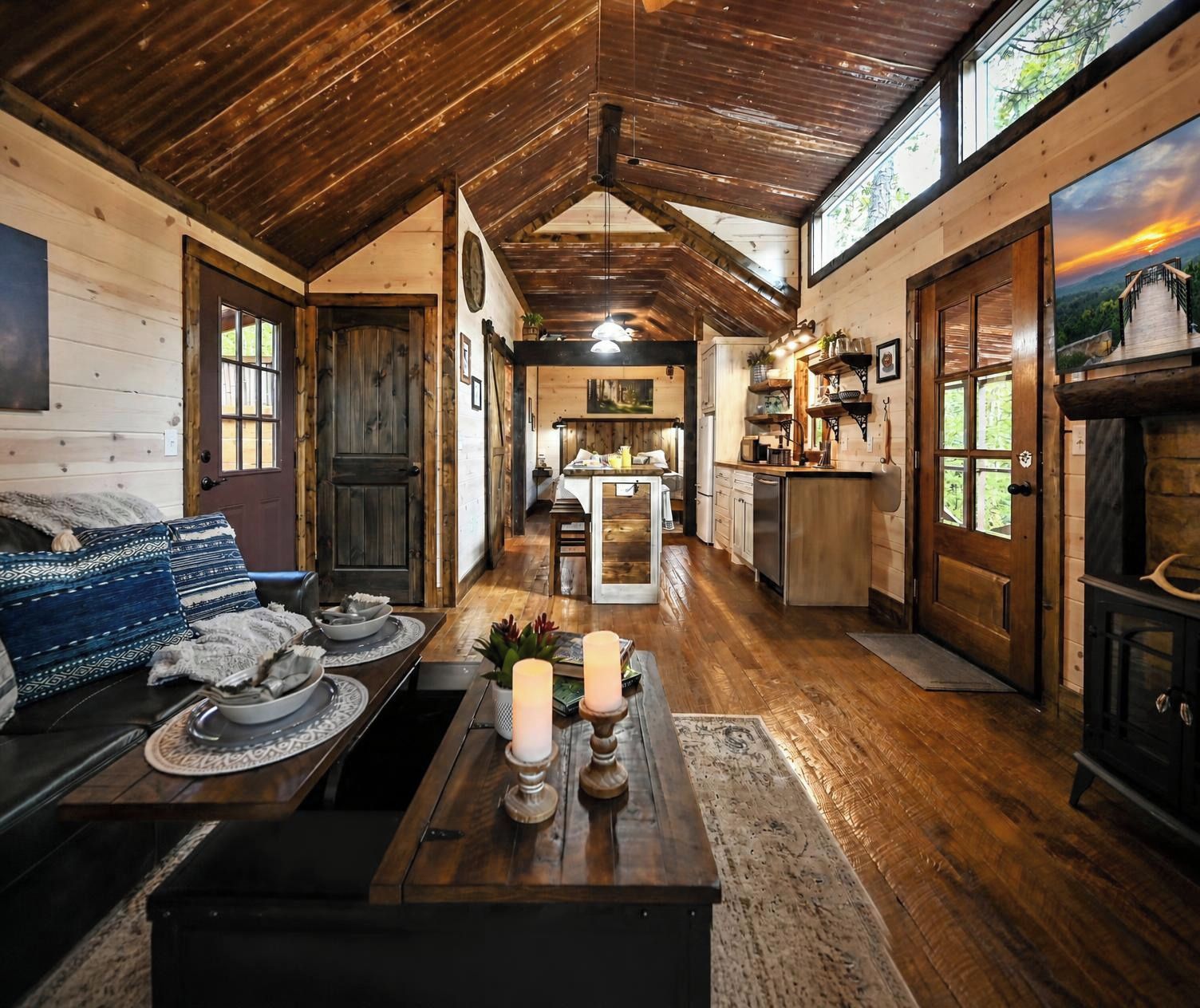 Ein gemütliches Blockhaushaus-Interieur mit Holzbalkendecke, einem Essbereich, einer Küche und einem Wohnzimmer mit Sofa und Kamin.