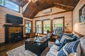 A cozy cabin interior with a fireplace, a television, and a comfortable seating area with a couch and a chair. - Cozy Couples Cabin/Private & Secluded/Hot Tub/Fire Pit/Hillside View (Broken Bow)