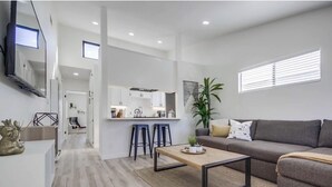Un soggiorno moderno con un divano grigio, un tavolino in legno e un'area cucina sullo sfondo.