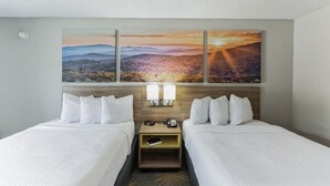 A hotel room with two beds, a nightstand, a lamp, and a painting of a landscape.