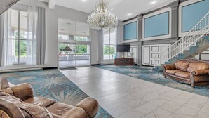 A spacious lobby with a chandelier, leather sofas, a staircase, and large windows offering a view of the outdoors.