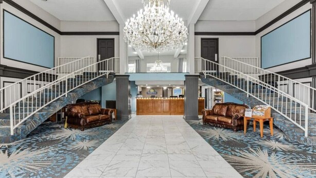 A spacious lobby with a grand chandelier, a reception desk, and a staircase leading to an upper level.