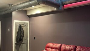 Une pièce avec un canapé en cuir rouge, une porte sur laquelle est accroché un manteau, et des conduits de ventilation qui courent le long du plafond.