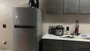 Une cuisine équipée d’un réfrigérateur en acier inoxydable, d’un four à micro-ondes et d’un évier. Des placards sont installés au-dessus du plan de travail, et une prise de courant se trouve sur le mur.
